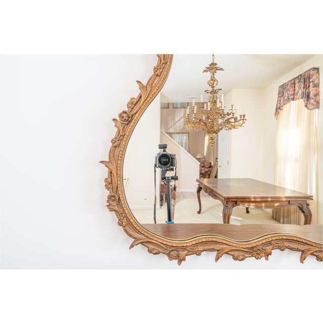 Striking large-scale carved gilt wall mirror in the French Rococo style, featuring an intricately detailed frame with...
