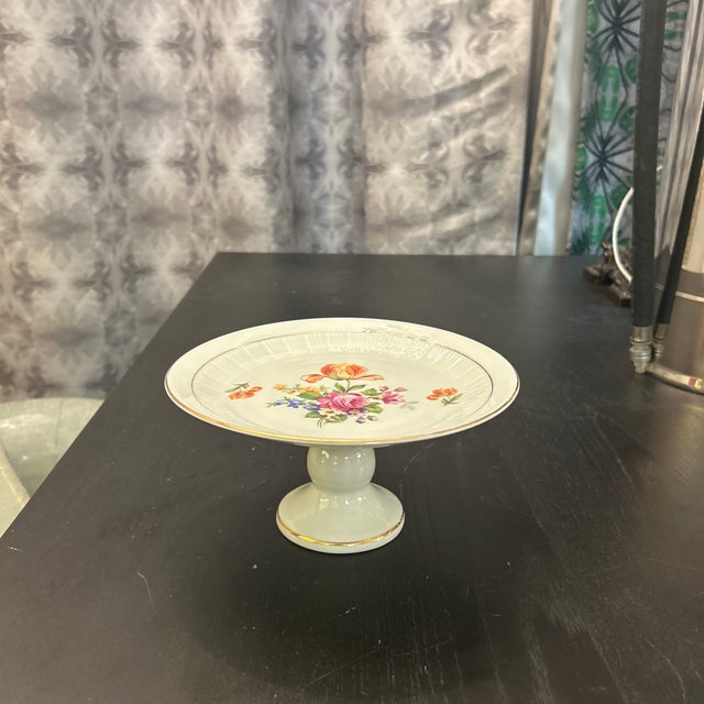 Wagner & Apel porcelain pedestal cake stand. It features a floral pattern with a textured border on the top surface. It is...