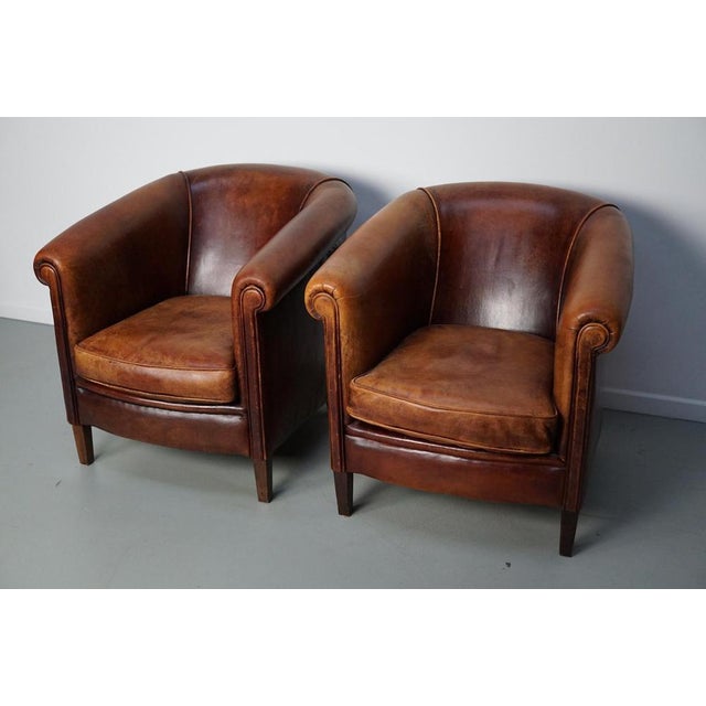This pair of cognac-colored leather club chairs come from the Netherlands. They are upholstered with patinated cognac-...