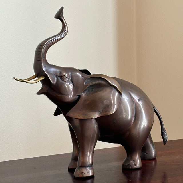 Vintage mid-century modern elephant sculpture featuring a rich bronze-tone finish with polished brass tusks. This striking...