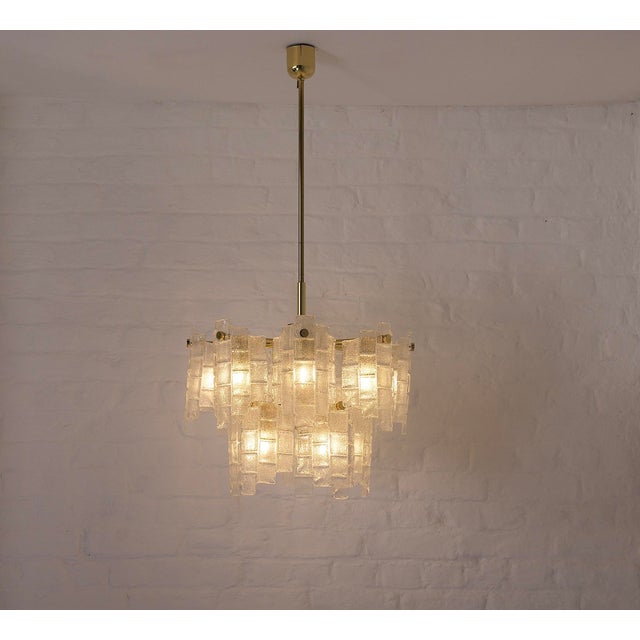 Brass chandelier composed of 13 light arms, each adorned with a curved, molded glass element with a compartmentalized...