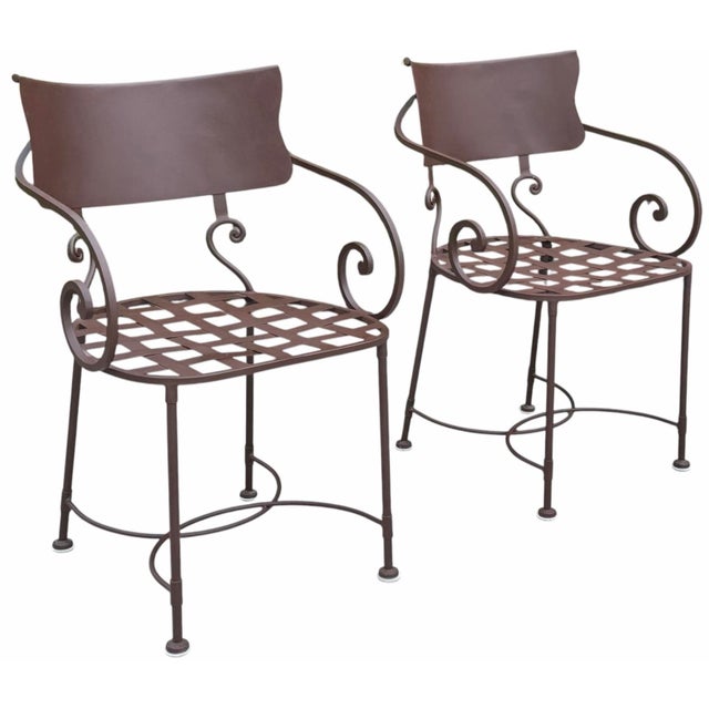 A handsome pair of vintage wrought iron garden dining armchairs featuring elegant scroll arms, lattice seats, and a...