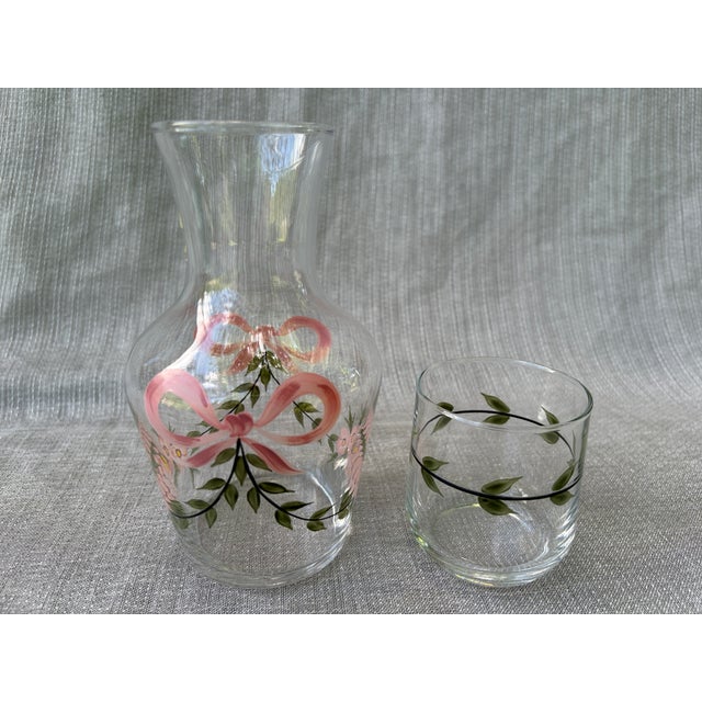 Sweet, vintage hand painted glass bedside carafe and cup set. Painted pink and green, bow, floral leaf design around both...