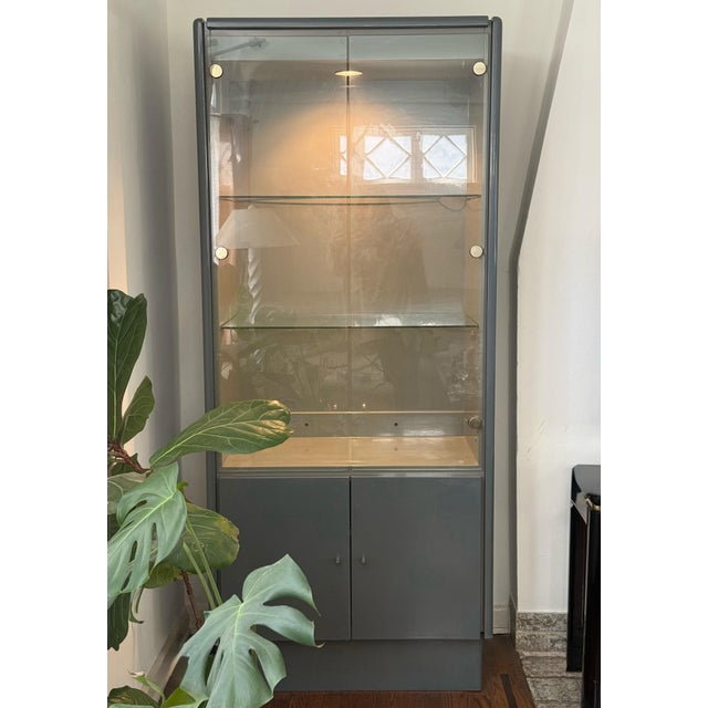 A postmodern display cabinet with interior light in rare gray lacquer and glass, late 20th century. With gold-toned...