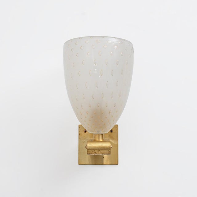An elegant pair of italian wall lamps with hand-blown murano glass lampshades in a delicate milky white hue. The glass is...
