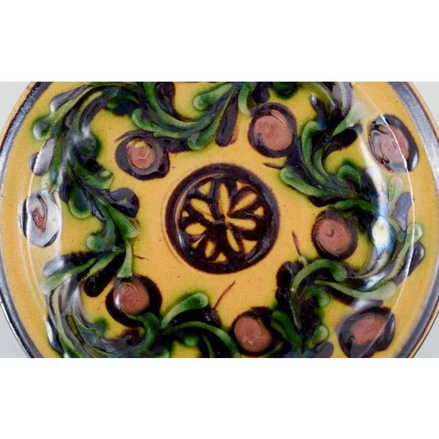 Kähler, Denmark. Dish/wall plaque made of ceramic with a floral motif. Glaze in green and black tones on an ochre-yellow...