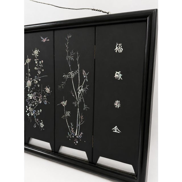 A striking vintage Chinese decorative screen featuring iridescent mother-of-pearl inlay against a deep black lacquer...