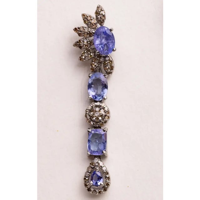 Unusual dangle earrings featuring oval and pear-shaped faceted Tanzanite gemstones with round, brilliant cut diamonds in a...