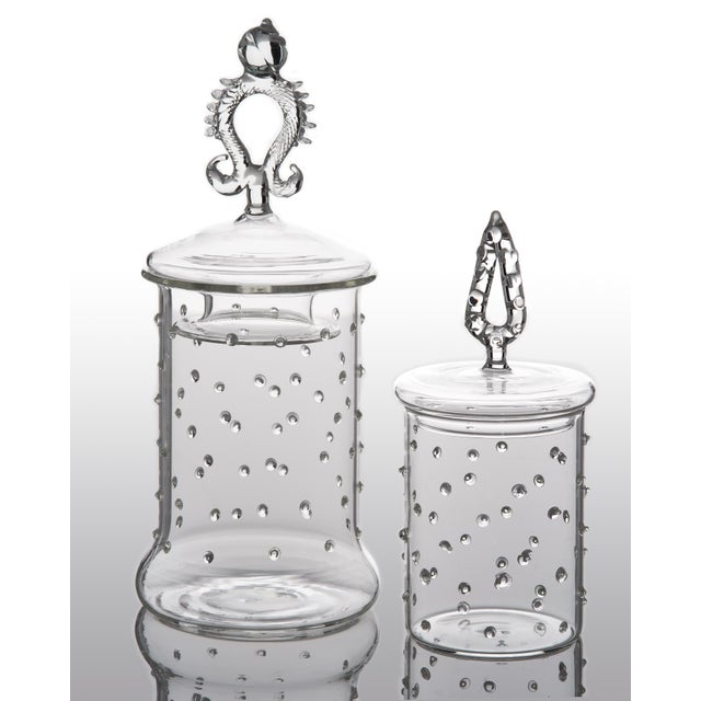 A set of two glass apothecary jars with decorative lids, one large and one small. Small glass dots are applied on the...