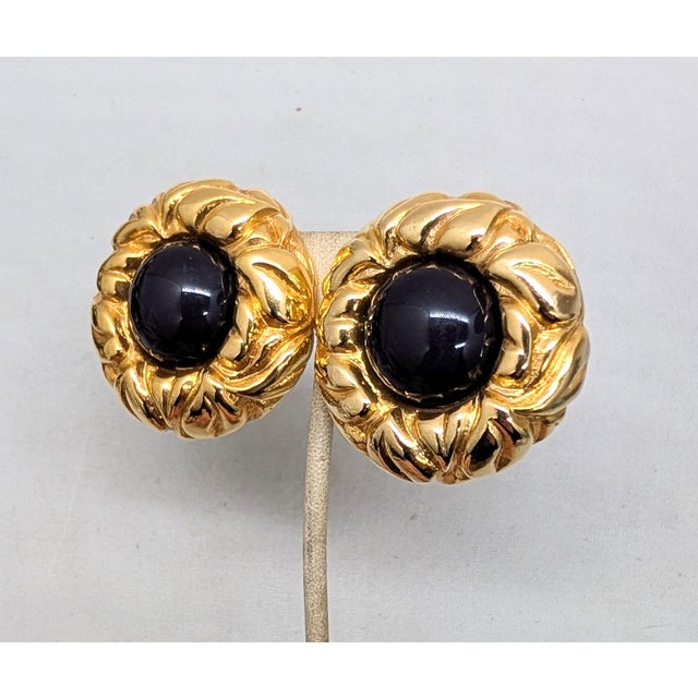 1980s round goldtone textured with cabochon faux-onyx center clip earrings. Marked "ESCADA©" on a cartouche on the back of...