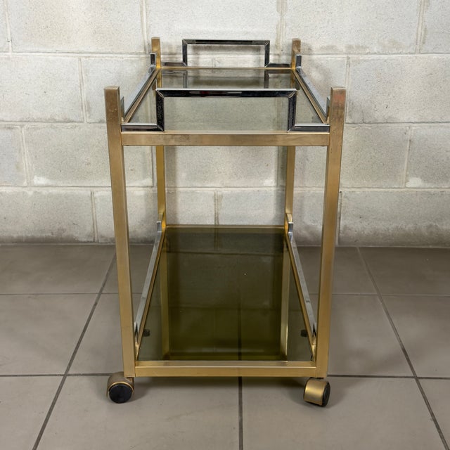 Prestigious and elegant two-tier bar cart in brass-plated metal, chrome finishes, and smoked glass shelves, a refined...