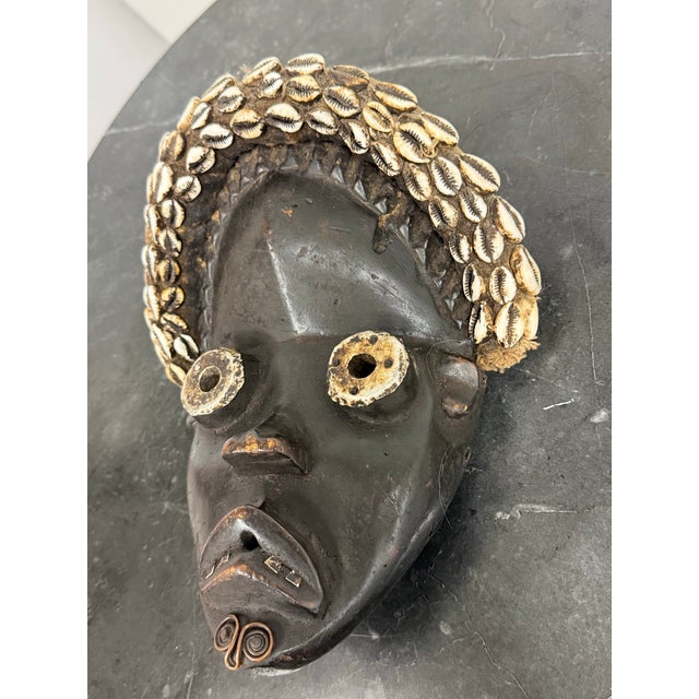 Design Plus Gallery presents a West African Dan Tribe Cowrie Shell Wood Mask. Carved from wood, the mask has an elongated...