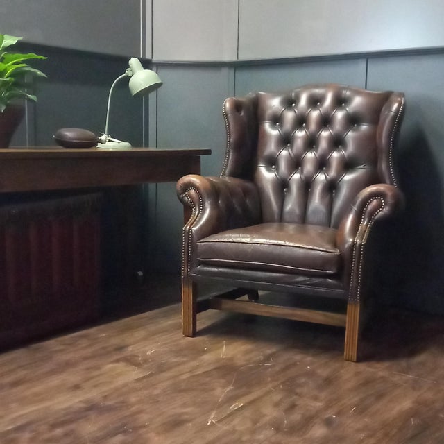 A high-quality English vintage wingback armchair in brown leather, executed in the George III style. The backrest,...