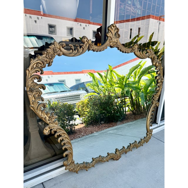 This oversize ornate piece is a French Provincial or Rococo-style gold wall mirror made in the 1960. An ornate, scalloped...