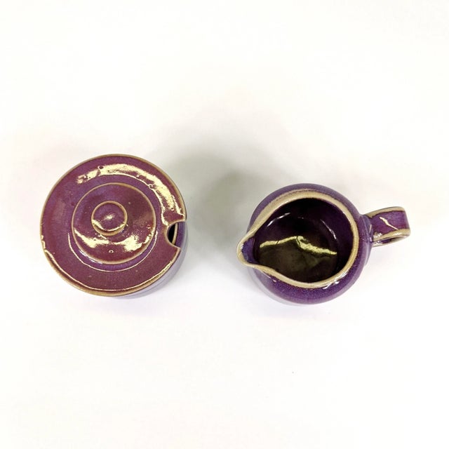 A mid-century purple glazed ceramic creamer and sugar. Artists signature at the bottom