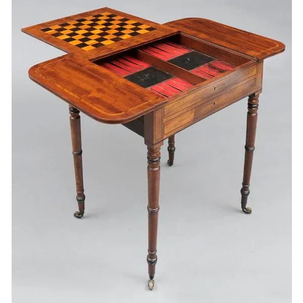Regency mahogany games table with two flaps, the top inlaid with a band of rosewood, the central sliding reversible top...