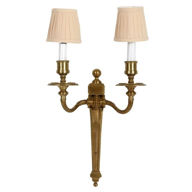 A pair of Neoclassical gilt wall sconces, each featuring two gracefully scrolled arms and candle-style sockets with a...