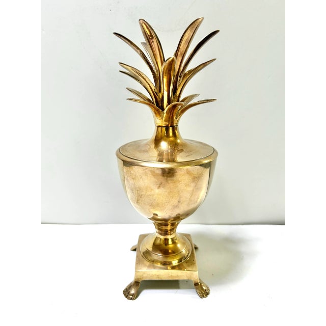 A classic Hollywood Regency brass pineapple urn featuring a removable lid and sculptural pineapple crown. The pineapple...