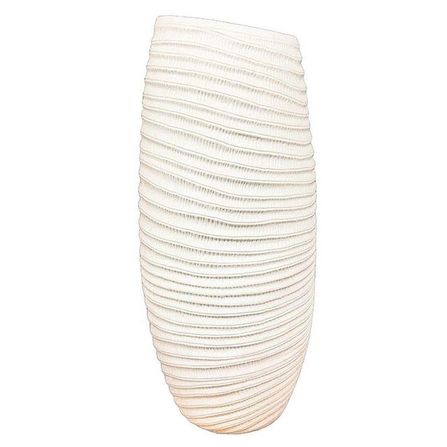 Ribbed Textured Coiled ceramic Vase by Bahari is a white, ribbed, barrel-shaped vessel, shaped with cascading ridges, and...
