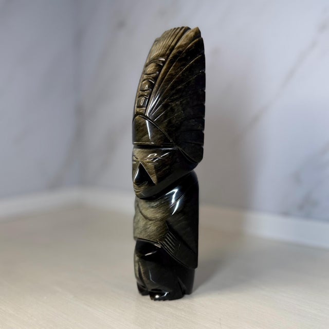 An 8‑inch (20 cm) hand‑carved figure in banded gold‑sheen obsidian from Mexico. The stylised form wears a feathered...