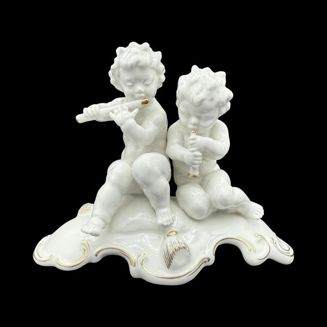 A pair of cherubs, caught mid-performance and full of easy charm. The two sit side by side atop a wave-like Rococo cloud...