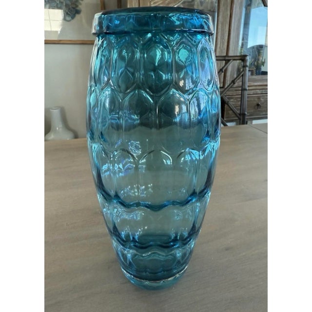 Lovely blown glass vase in a teal blue color. It stands 11” tall and is 4.5” wide. The glass at the top is rolled over to...
