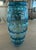 Lovely blown glass vase in a teal blue color. It stands 11” tall and is 4.5” wide. The glass at the top is rolled over to...