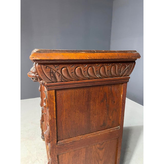 This ornate carved wooden cabinet features two paneled doors, two upper drawers, and an elaborately decorated facade. The...