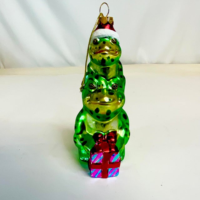 This Mercury Glass Christmas Ornament is two stacking frogs with a Christmas present. The smaller frog on top is wearing a...
