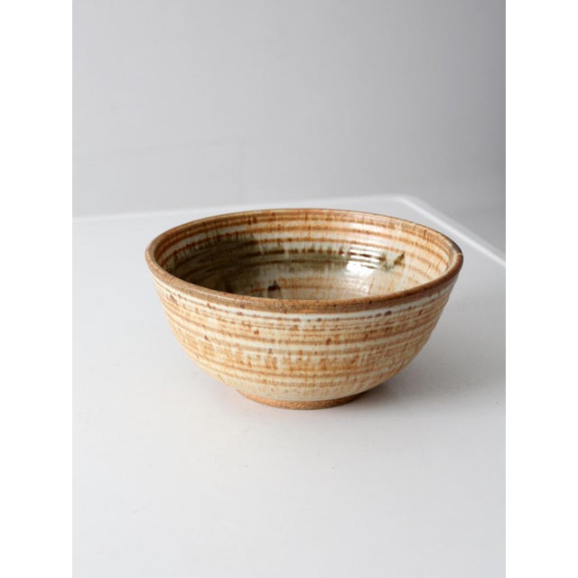 This vintage handmade studio pottery serving bowl features a wheel-thrown form with softly ribbed sides and layered cream,...