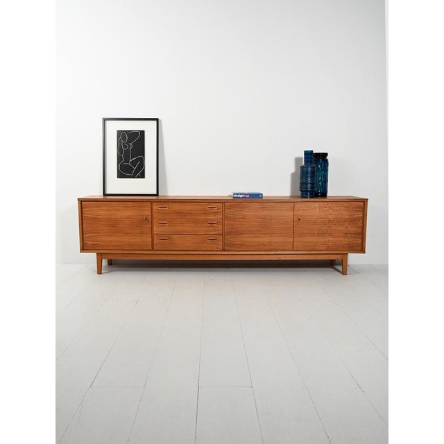 German-made walnut sideboard from the 1960s, with three doors and drawers: warm grain, horizontal lines, and low carved...