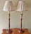 A pair of wooden candlestick lamps, topped with solid brass cups and handsomely pleated custom-made shades. The wood bases...