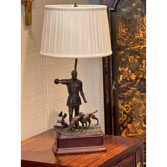 A table lamp with a bronze figural group as the base — a huntsman in riding dress sounding a horn, with two hounds and a...