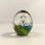 Oval shaped, artisan-made, hand-blown, Italian Murano art glass paperweight features a bed of colorful teal, blue, yellow,...