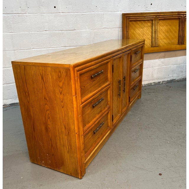 Vintage Lea Furniture faux bamboo credenza features a warm wood laminate finish, central woven-rattan cabinet doors, and...
