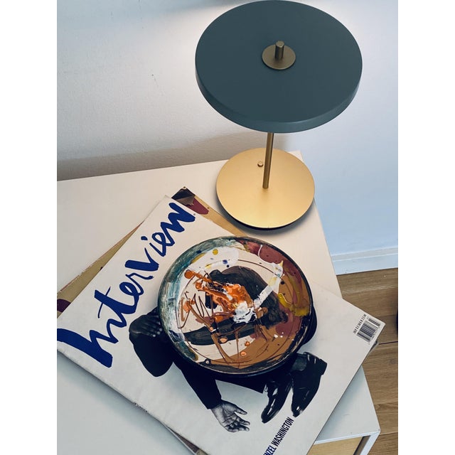 Bold gestural marks in orange, black and earth tones sweep across a cream ground — punctuated by splashes of cobalt blue...