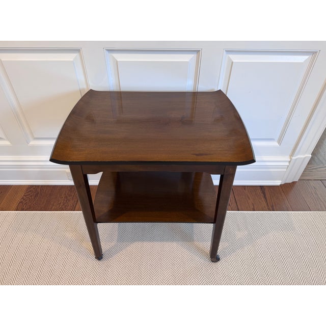 Handsome two-tier side or serving table featuring warm walnut-toned wood and elegant, clean-lined construction. The table...