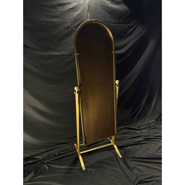 A distinctive freestanding cheval mirror frame featuring an elongated arched form, gold-tone metal construction, and...