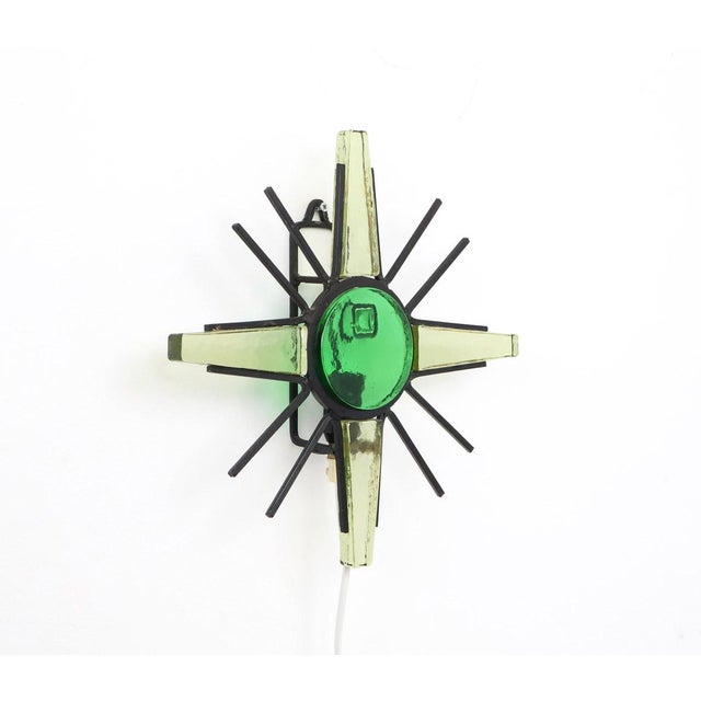 Black metal sunburst wall lamp with green glass, 1960s This unique wall lamp features a powerful sunburst shape, where...