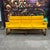 This mid-century modern sofa features a mustard yellow fabric with channeling along the back rest and arms. The frame and...