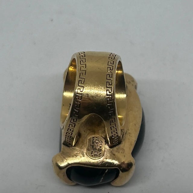 This Gianni Versace cocktail ring features a bold design with a large, oval-shaped black agate (as the centerpiece. The...