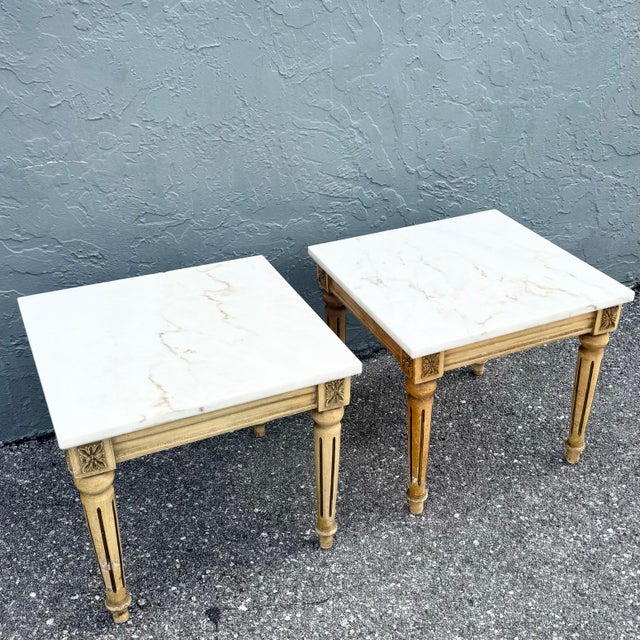 An elegant pair of neoclassical side tables, featuring solid wooden frames topped with refined marble surfaces. The bases...