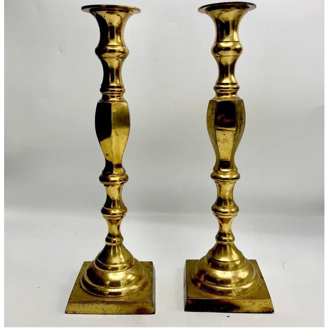 An elegant pair of tall, lacquered brass candlesticks featuring graceful, architectural silhouettes and the understated...