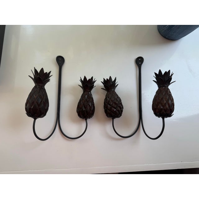 Pair of decorative wall hangings featuring hand-carved wood pineapple forms with wrought iron leaves and scrollwork....