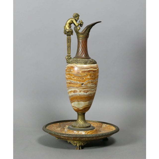 Brown and white banded onyx, with bronze details, animal feet and a horned figure holding a bunch of grapes.