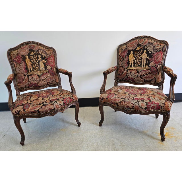 A pair of French Louis XV style Fauteuils features walnut frame with carved foliate, floral and scroll decoration;...