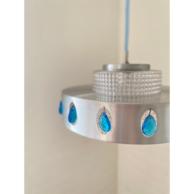 Vitrika pendant lamp with a distinctive mid-century design. The aluminum housing is accented with elegant blue decorative...