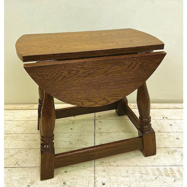 A small Mid-Century Oak drop-leaf table with turned legs and side stretchers. This Brutalist-style side table features two...
