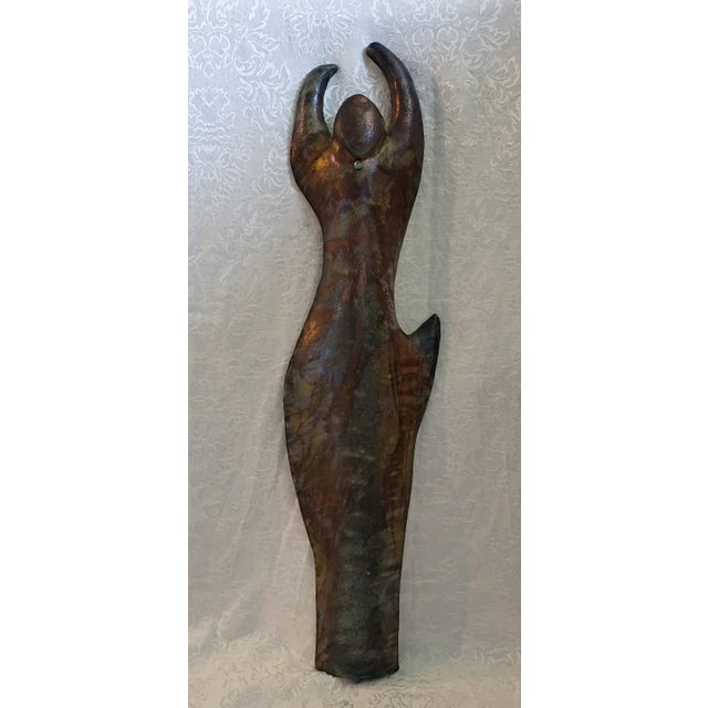 This authentic figurative piece features a stylized, fluid female form with arms raised in an abstract silhouette....