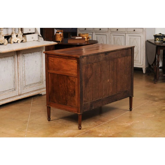 A French Louis XVI period walnut commode circa 1790 with three drawers, linear brass hardware, cylindrical tapered legs...